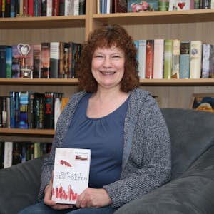 Eine Frau hält lächelnd ein Buch mit dem Titel „Die Zeit des Poeten“ in den Händen.