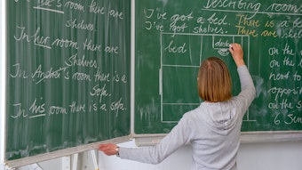 Eine Englisch-Lehrerin an der Tafel, sie schreibt mit Kreide in Englisch.