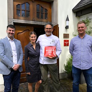 Vier Personen stehen vor einem Gebäude mit einer großen Holztüre. Ein Mann hält eine rote Plakette mit der Michelin-Auszeichnung in der Hand.&nbsp;