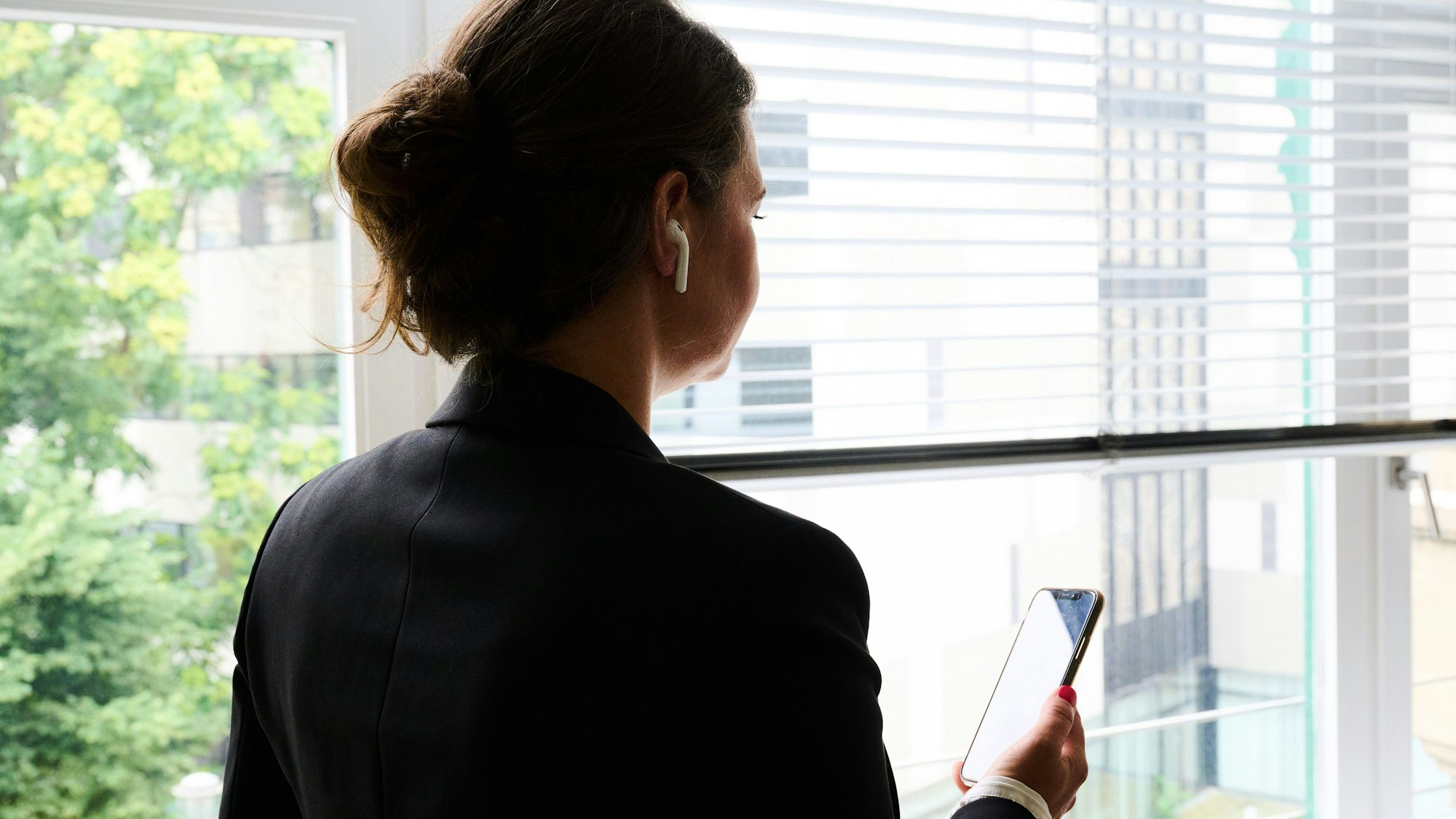 Eine Frau steht in einem Bürozimmer am Fenster und telefoniert über ein Headset. (gestellte Szene)