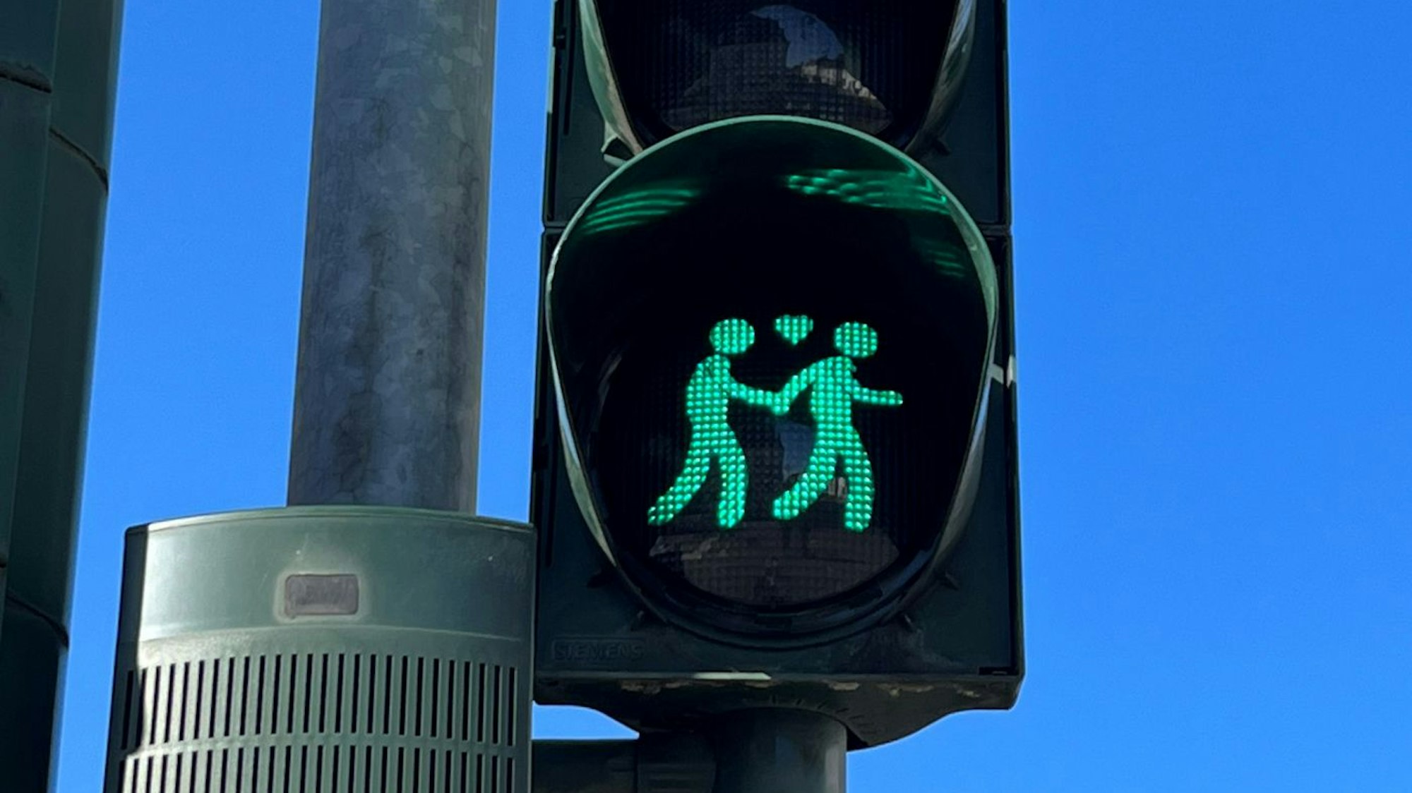 Das Foto zeigt eine Ampel mit einem gleichgeschlechtlichen Paar, zwischen ihnen befindet sich ein Herz. Die beiden Figuren leuchten grün.