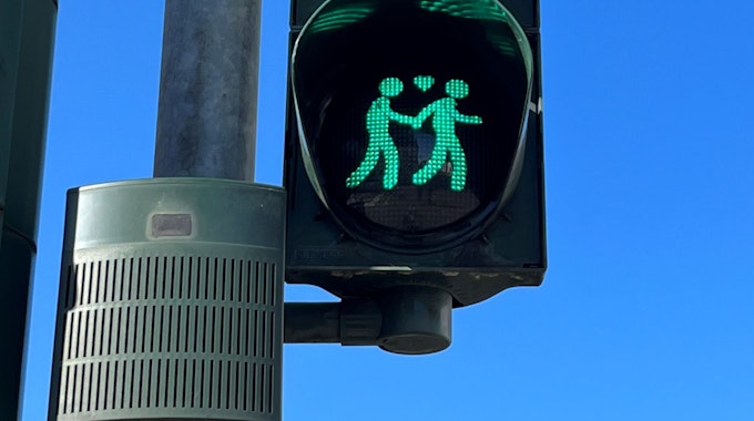 Das Foto zeigt eine Ampel mit einem gleichgeschlechtlichen Paar, zwischen ihnen befindet sich ein Herz. Die beiden Figuren leuchten grün.