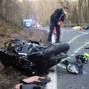 Nach einem Unfall in Much am 20. Februar 2021 liegen Teile eines Motorrads auf der Straße. Ein Polizist sichert die Szene.