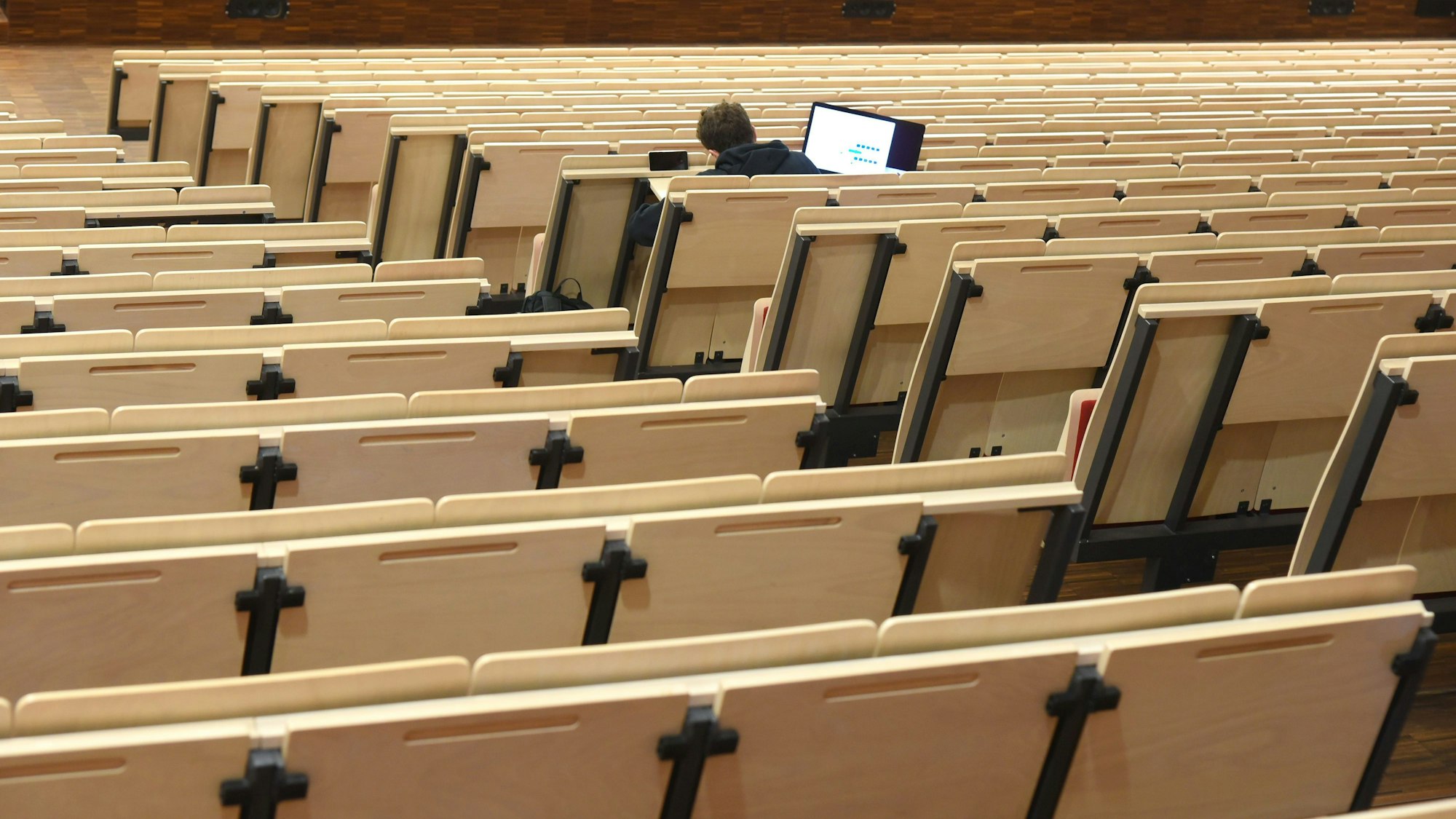 Ein Student sitzt in einem ansonsten leeren Vorlesungssaal.