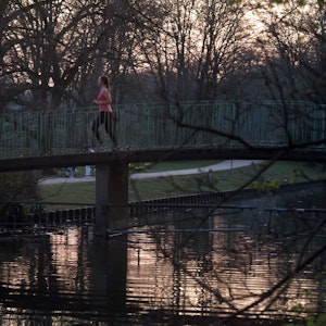 Frau läuft im Kölner Stadtwald über eine Brücke am Kahnweiher.