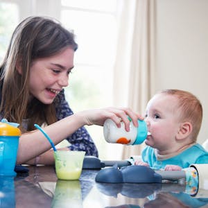 Ein Mädchen gibt einem Baby am Tisch eine Flasche.