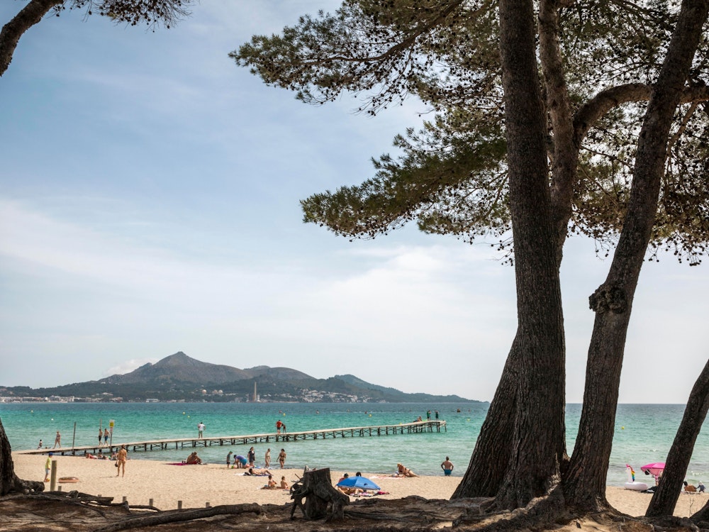 Menschen liegen in der Sonne vor dem Meer am Playa de Muro, hier im Juni 2021, auf Mallorca.