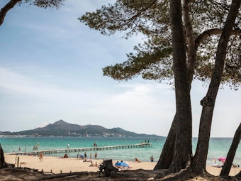 Menschen liegen in der Sonne vor dem Meer am Playa de Muro, hier im Juni 2021, auf Mallorca.