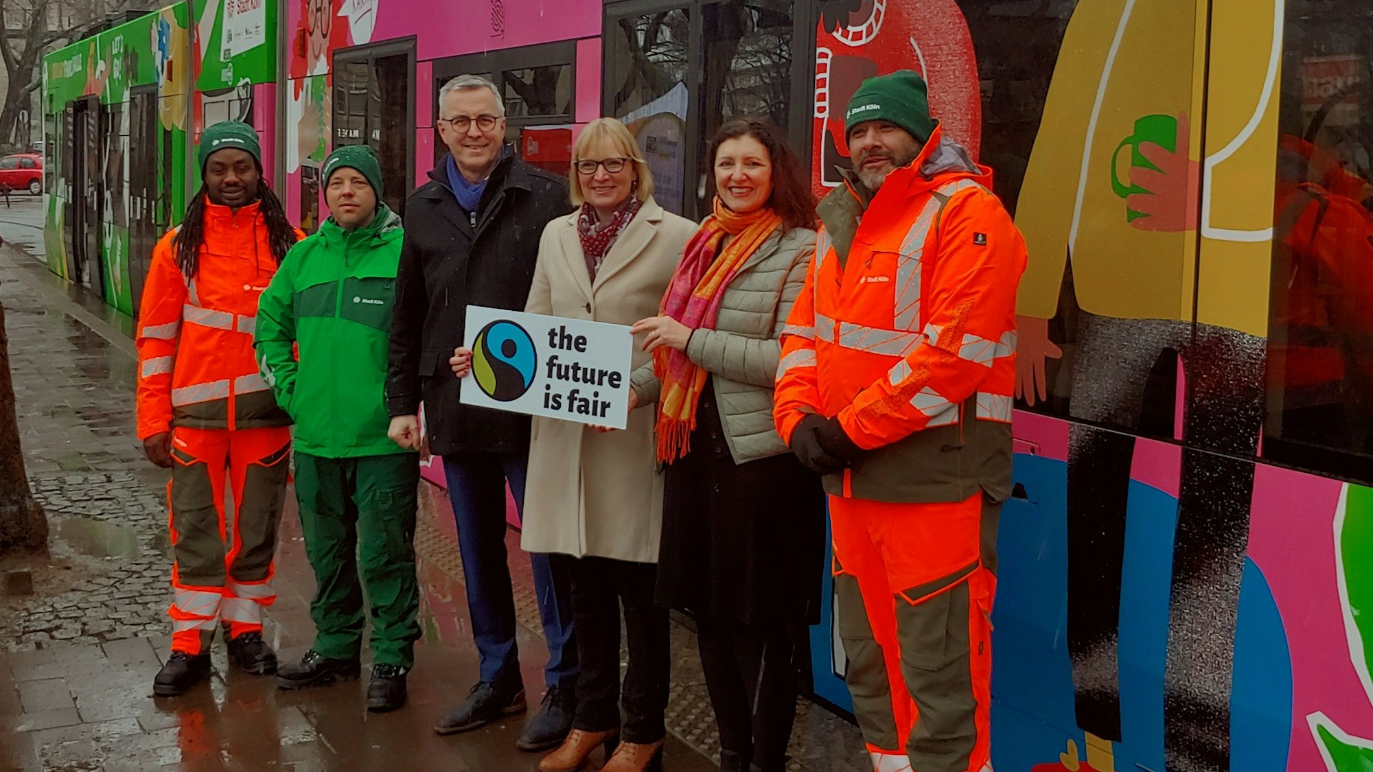 Sechs Personen, die mit einem „The future is fair“-Schild vor einer bunt gestalteten Straßenbahn stehen
