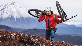 Tobias Woggon trägt sein Mountainbike einen Berg hinauf.