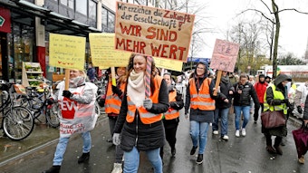 Eine Demonstrantin trägt ein Schild mit der Aufschrift "Wir erziehen die Zukunft der Gesellschaft. Wir sind mehr wert!" auf einer Demo für mehr Lohn in Sozialberufen in Köln.