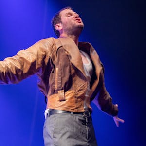 Sänger Marco Michael Wanda von der Band Wanda im Konzert in der Innsbrucker Olympiahalle im Juni 2022. Er hat die Arme aus- und die Brust vorgestreckt und trägt seine abgewetzte braune Lederjacke.