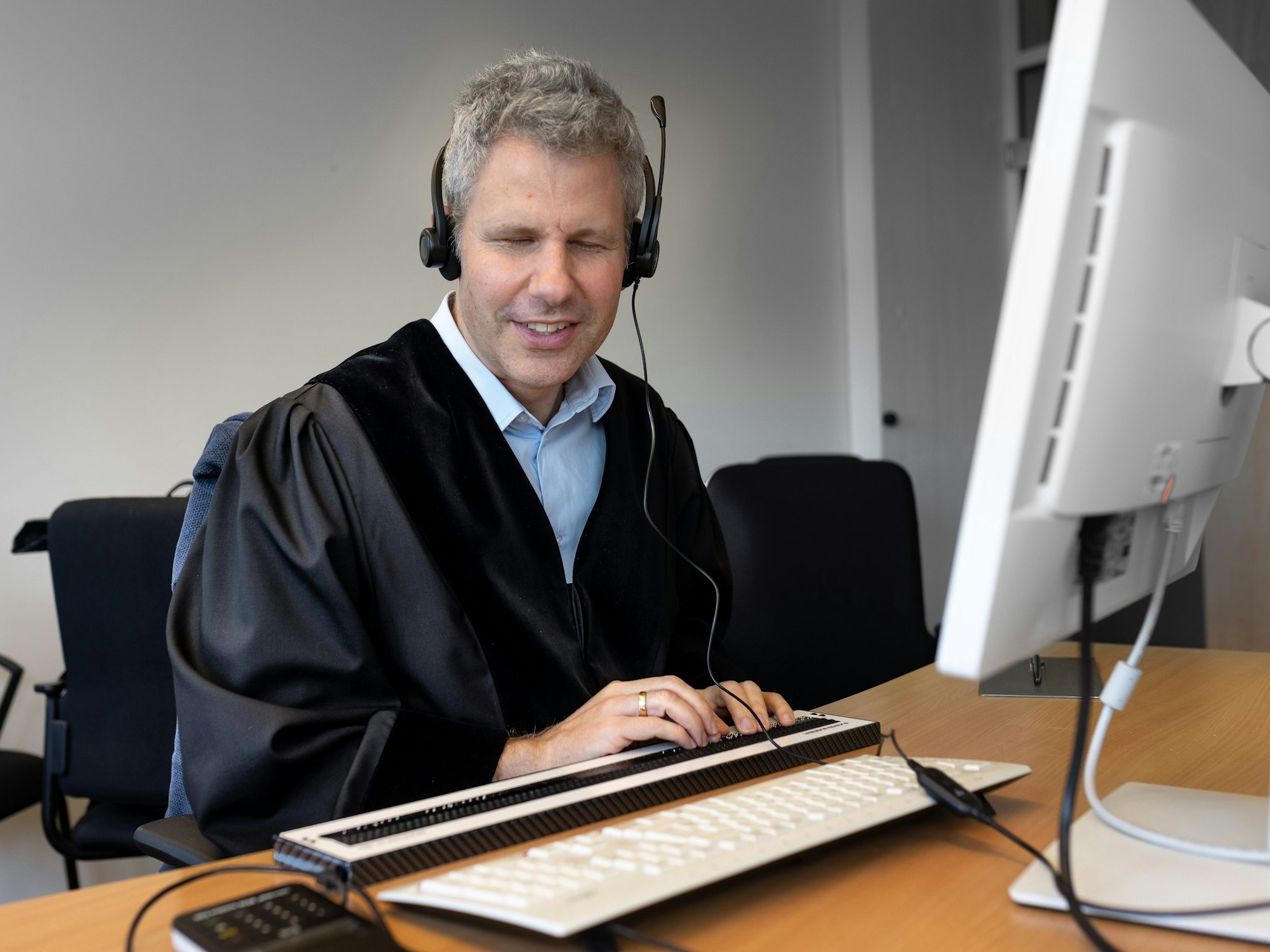 Der blinde Jurist Ulrich Badde sitzt an seinem Computer-Arbeitspatz mit einer Blindentastatur.
