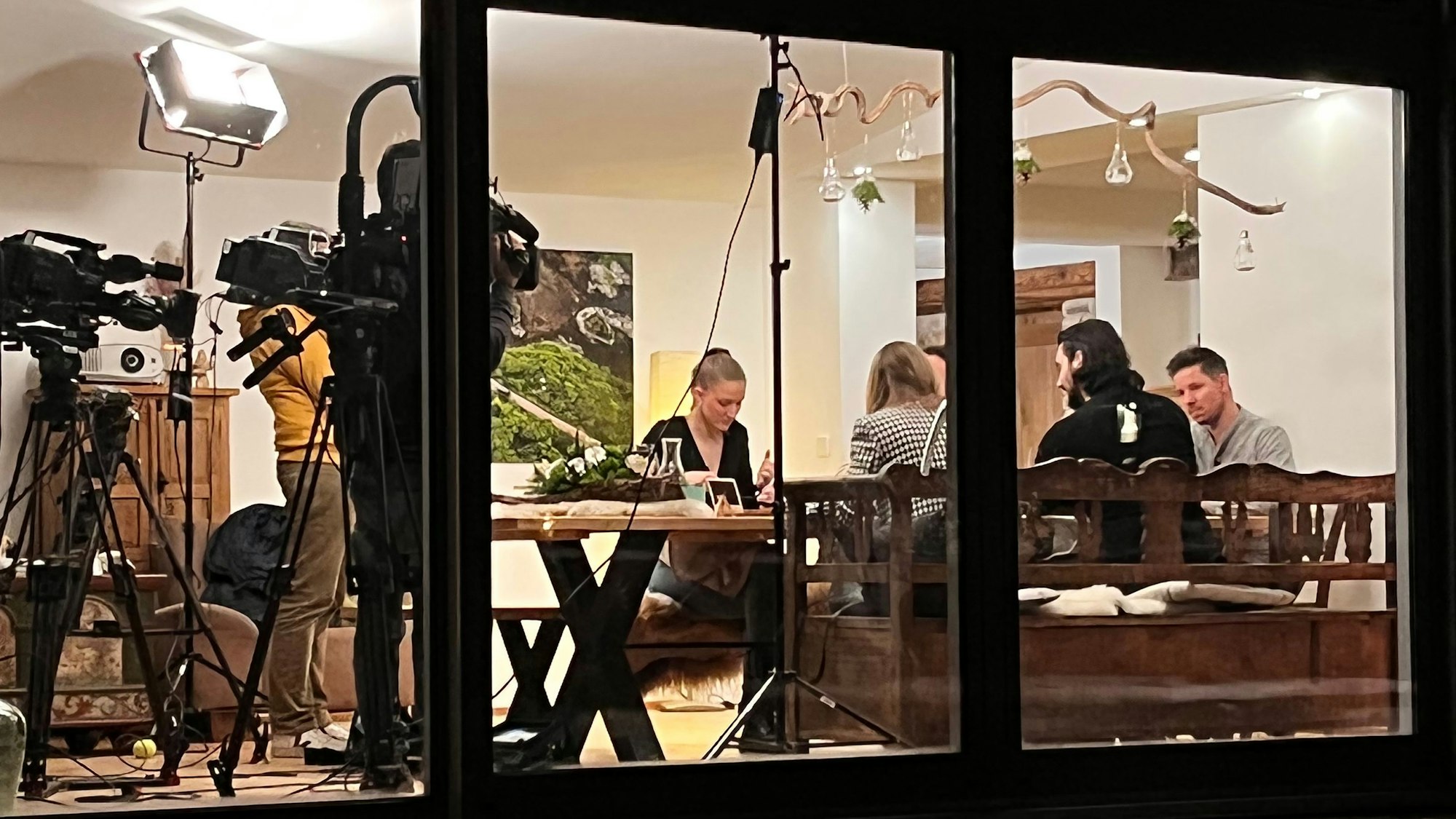 An einem Tisch sitzen mehrere Personen daneben stehen zwei Personen mit einer Kamera und filmen den Tisch.