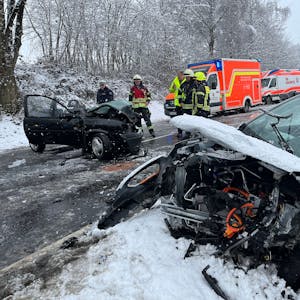 Ein völlig zerfetztes Auto liegt auf der Straßenseite im Schnee, quer auf der Straße steht ein anderer, ebenfalls schwer beschädigter Pkw. Mehrere Feuerwehrleute, Polizisten und Rettungsfahrzeuge stehen auf der winterlichen Straße.
