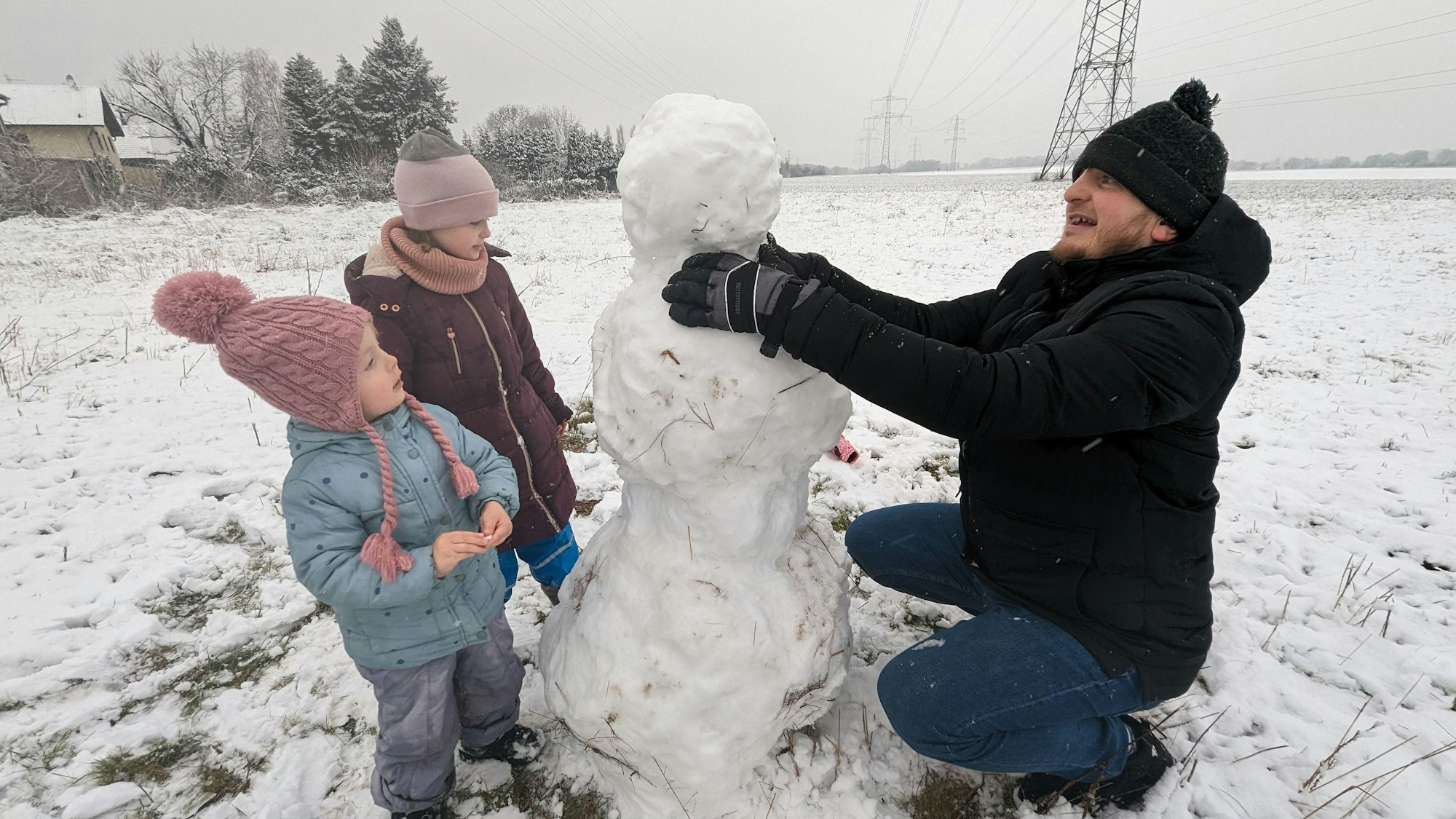 Zwei Kinder und ein Mann bauen einen Schneemann