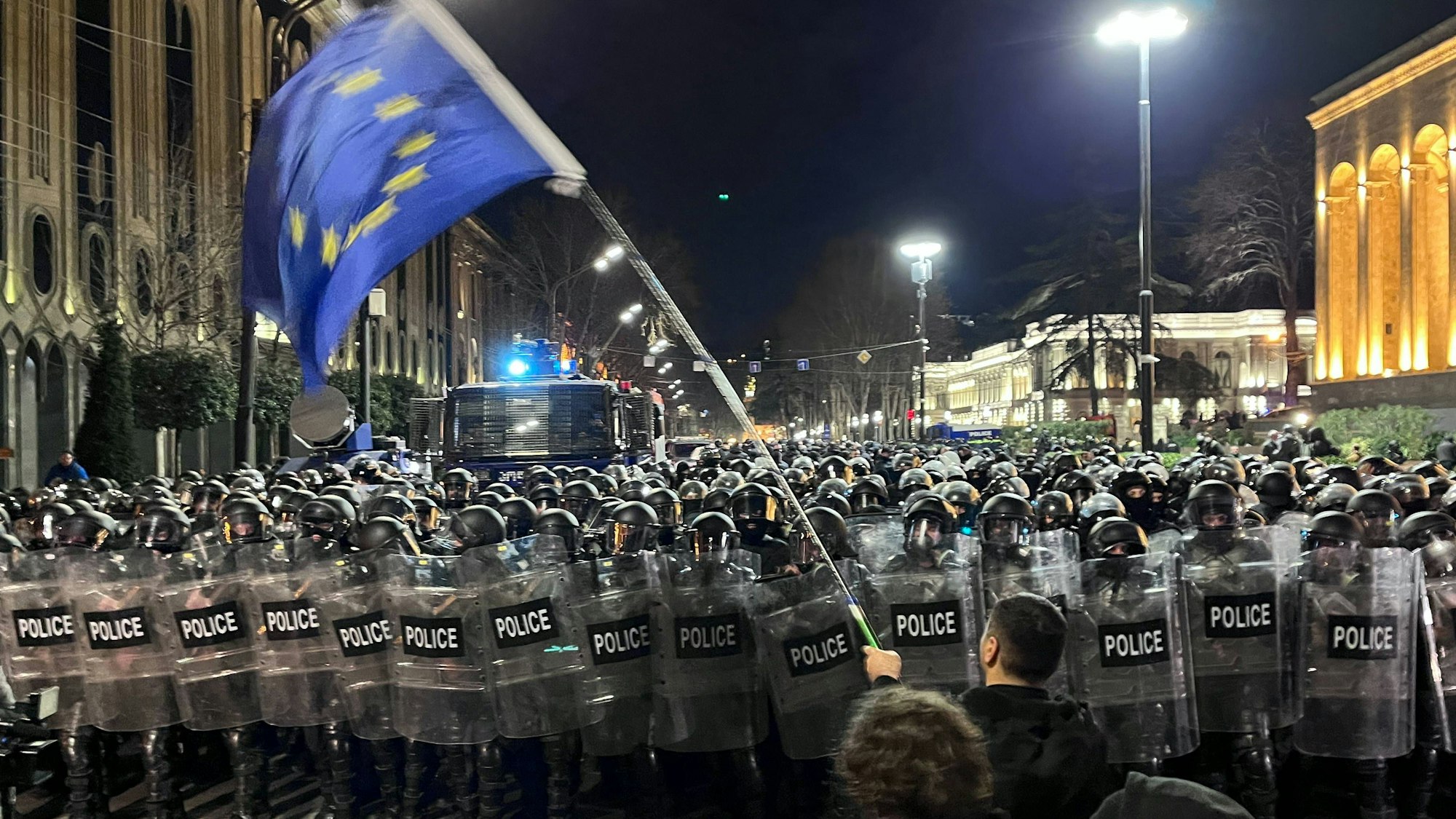 Ein Demonstrant, der eine EU-Flagge trägt, geht auf eine Polizeikette vor dem georgischen Parlamentsgebäude zu. Unter heftigem Protest aus der Bevölkerung ist in Georgien im Südkaukasus eine umstrittene Regelung über „ausländische Agenten“ auf den Weg gebracht worden.