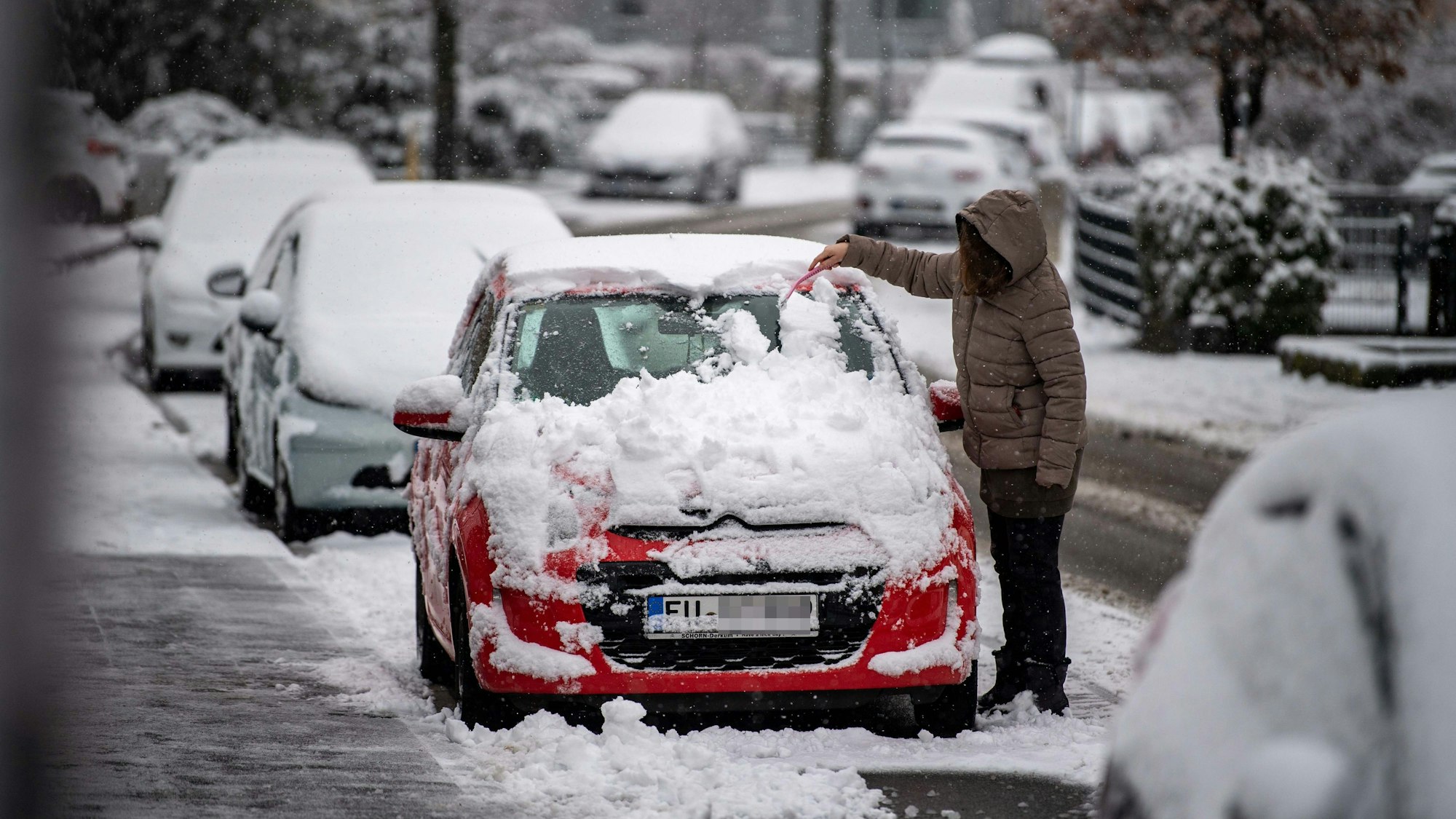 Das Bild zeigt eine Frau, die ihr rotes Auto vom Schnee befreit.