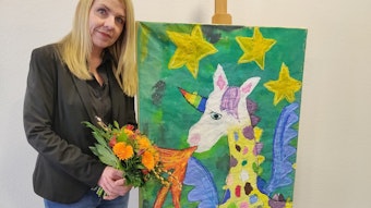 Aleksandra Petz steht mit einem Blumenstrauß neben einem Tierbild, das Kinder der Grundschule Büscherhof gemalt haben.