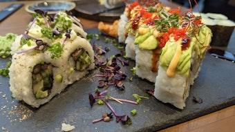 Verzierte Sushi-Rollen mit Reis stehen auf einer schwarzen Schieferplatte.
