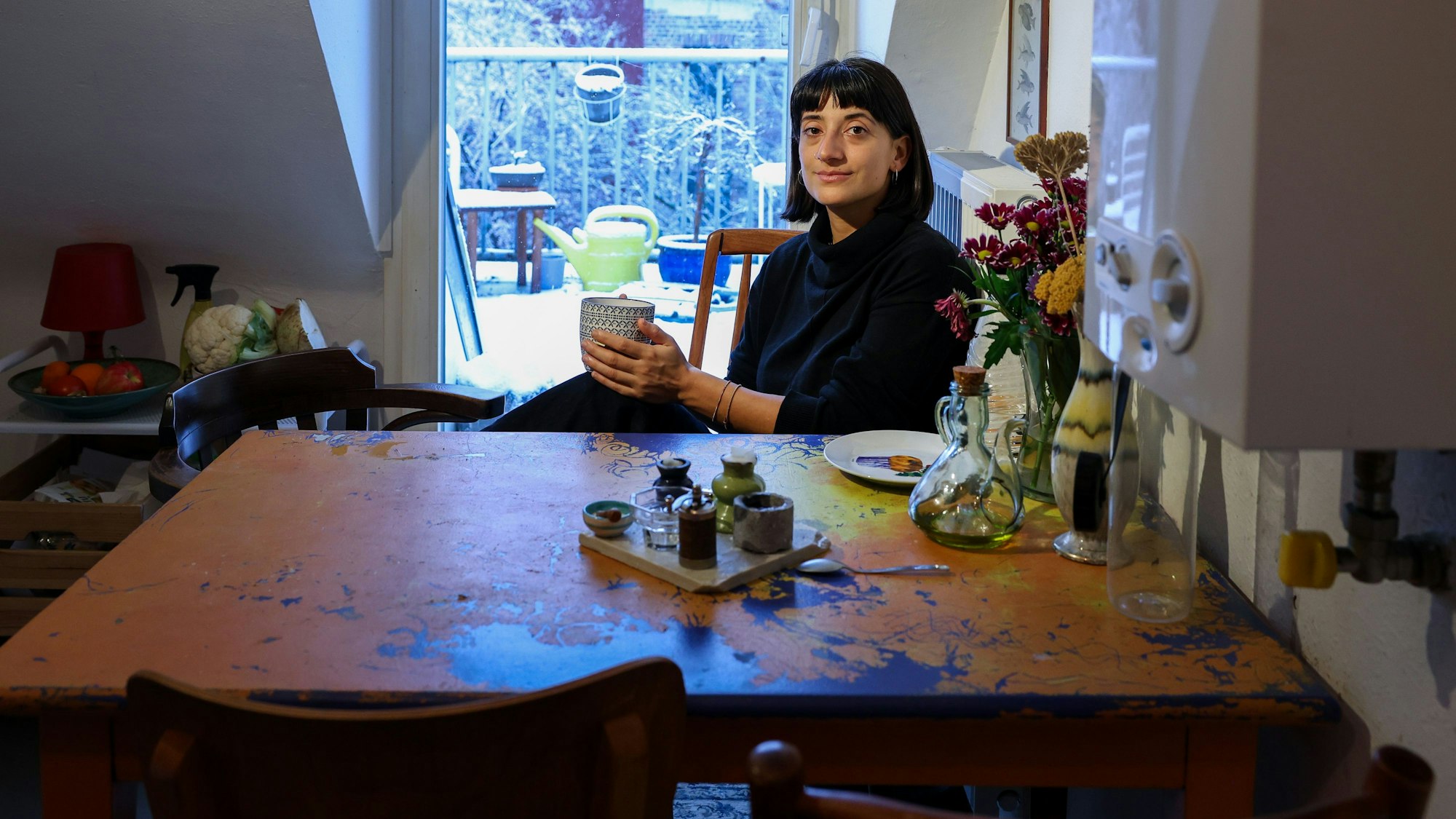Deniz Kideys sitzt
in der Küche ihrer WG und hält eine Tasse in der Hand.
