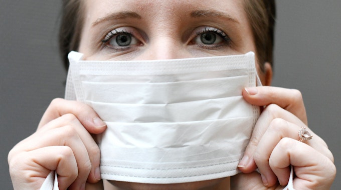 Eine Frau hält einen Mundschutz vor ihrem Gesicht.