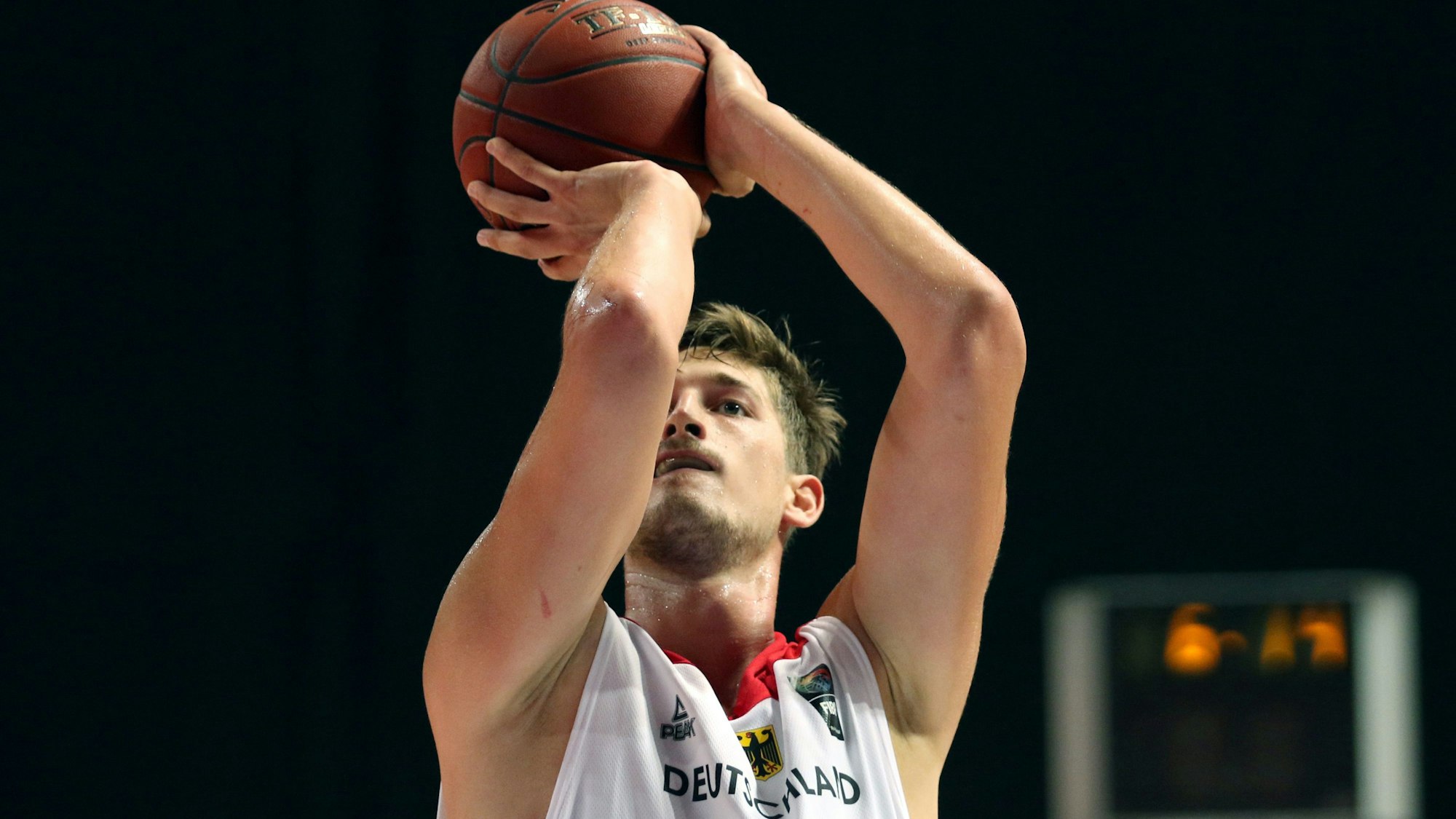 Tibor Pleiß hat einen Basketball in seinen Händen, die Arme über den Kopf gestreckt.
