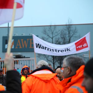 Streikende stehen mit einem Banner mit der Aufschrift „Warnstreik“ vor dem Werkstor der AWB Abfallwirtschaftsbetriebe.