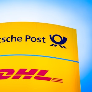Die Logos von Deutsche Post und DHL leuchten am Morgen auf einem Schild vor einer Zustellbasis.