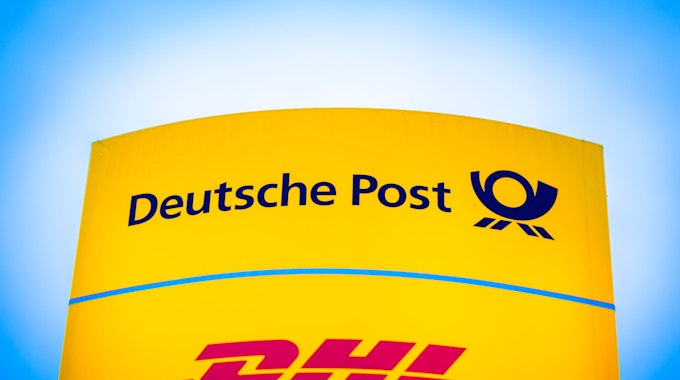 Die Logos von Deutsche Post und DHL leuchten am Morgen auf einem Schild vor einer Zustellbasis.