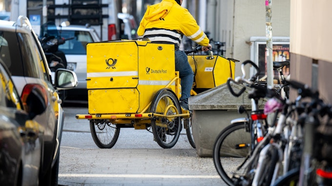 Ein Briefträger fährt mit seinem Fahrrad eine Straße in München entlang. Bei der Deutschen Post gehen die Verhandlungen zwischen Arbeitgebern und Verdi nach einem klaren Streik-Votum an diesem Freitag weiter.