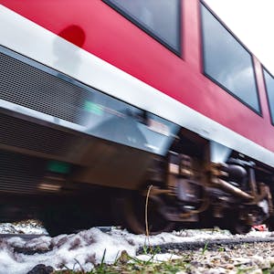 Ein rot-weißer Regionalzug rauscht über Bahnschienen.&nbsp;