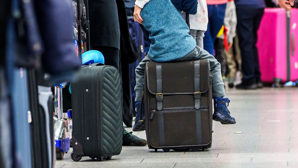 Ein Kind sitzt in einer Warteschlange am Flughafen in Frankfurt am Main auf seinem Koffer.