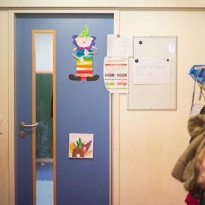 Kindergarten im Kreis Euskirchen. Tür mit Bildern, am rechten Rand hängen Jacken und Rucksäcke.