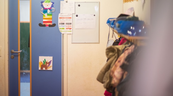 Kindergarten im Kreis Euskirchen. Tür mit Bildern, am rechten Rand hängen Jacken und Rucksäcke.