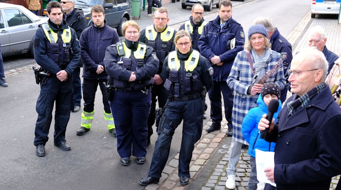 Polizistinnen und Polizisten sowie Menschen in ziviler Kleidung stehen auf einer Straße und hören Michael Heinen zu.