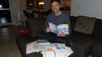 Andreas Stenschke sitzt auf dem Sofa und hält sein Lernbuch in der Hand