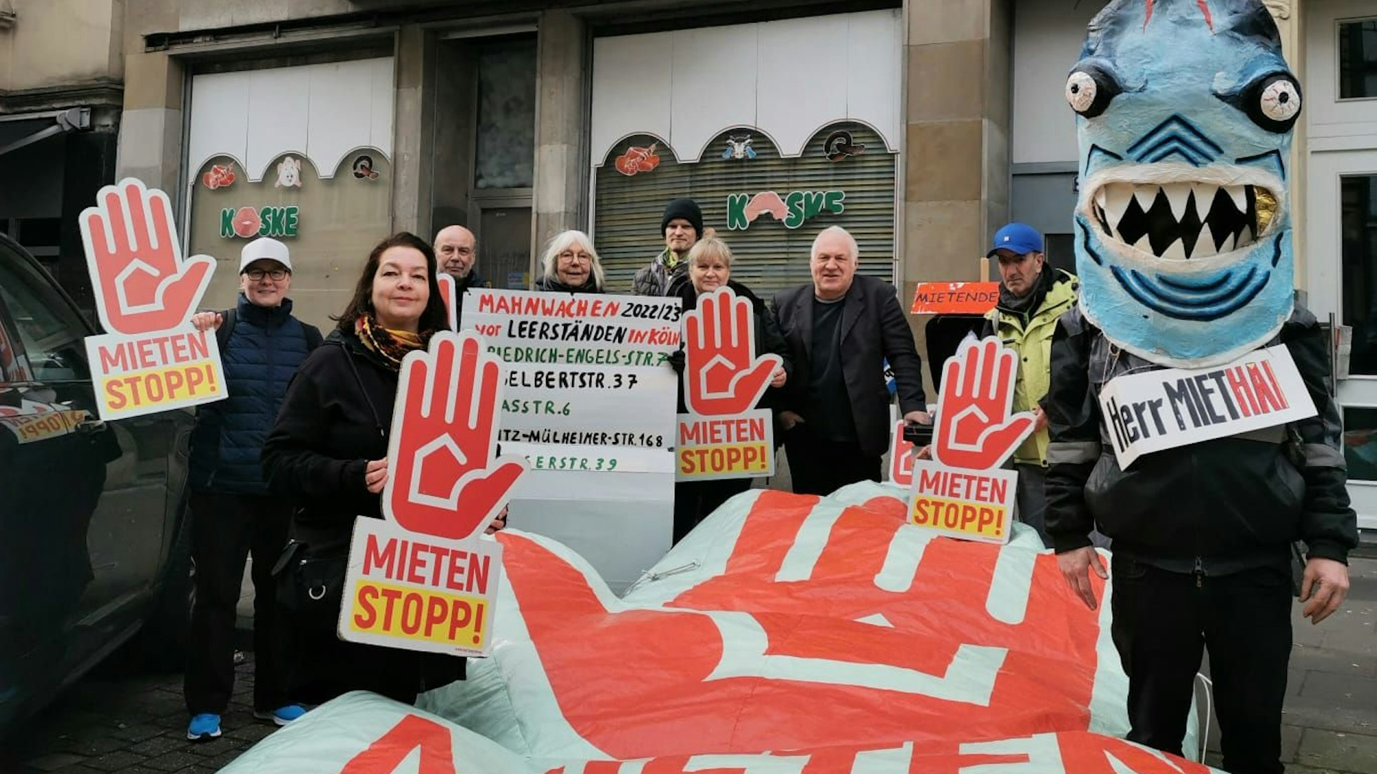 Mehrere Personen stehen mit Plakaten mit der Aufschrift „Mietenstopp!“ vor einem Haus.