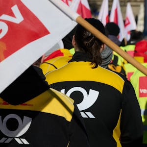 Mitarbeiter und Mitarbeiterinnen der Deutschen Post beteiligen sich auf dem Friedensplatz in Dortmund an einer Kundgebung. Sie tragen gelb-schwarze Post-Kleidung und eine rot-weiße Verdi-Fahne ist zu sehen.