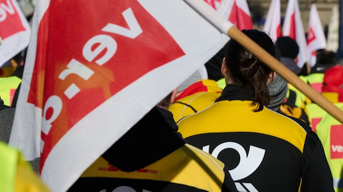 Mitarbeiter und Mitarbeiterinnen der Deutschen Post beteiligen sich auf dem Friedensplatz in Dortmund an einer Kundgebung. Sie tragen gelb-schwarze Post-Kleidung und eine rot-weiße Verdi-Fahne ist zu sehen.