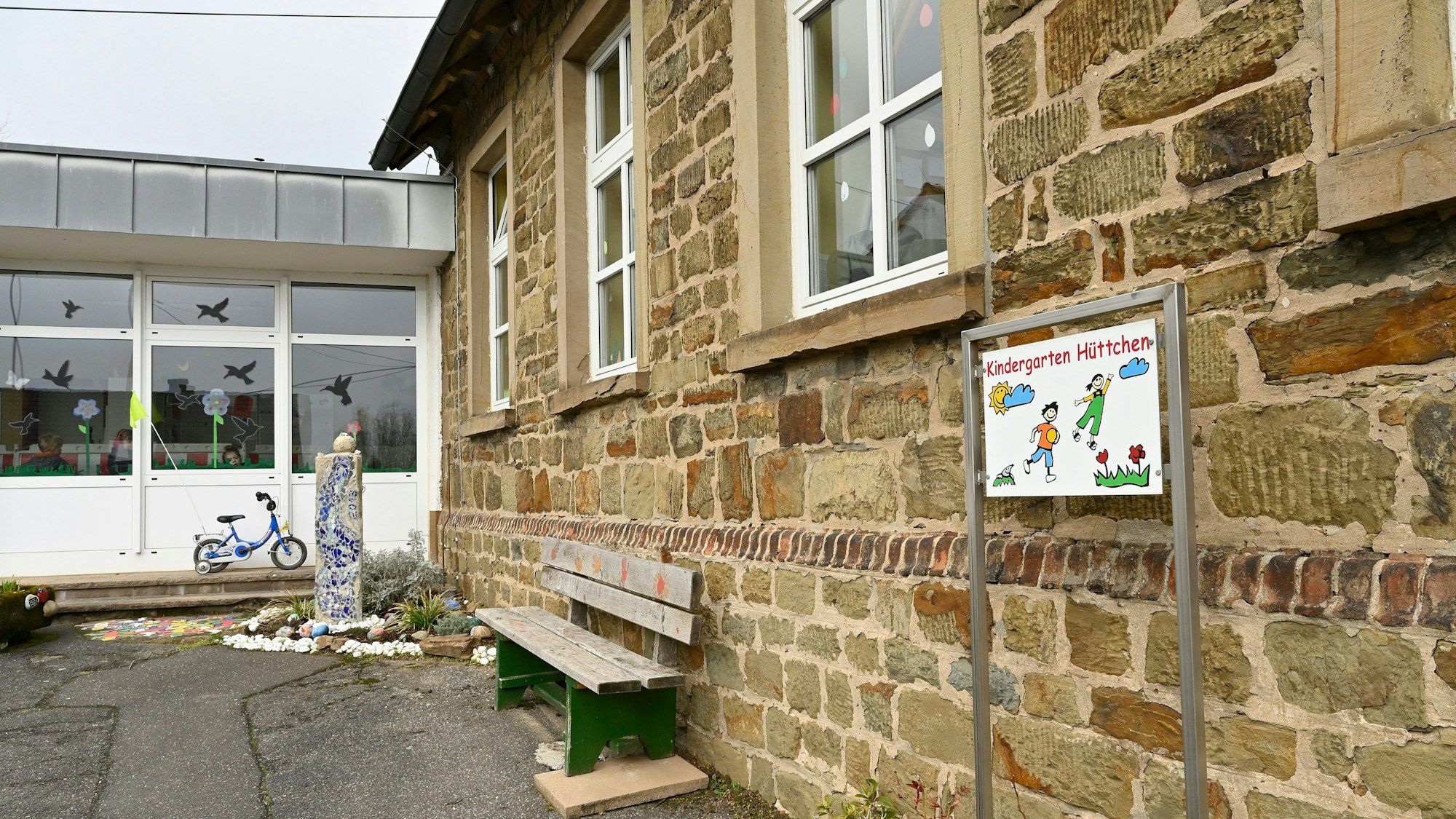 Kindergarten Odenthal-Hüttchen, Altbau mit Anbau, davor eine Sitzbank.