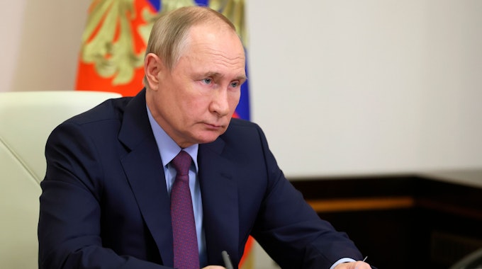 Wladimir Putin sitzt an einem Schreibtisch und hält ein Blatt Papier