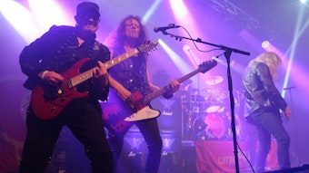 Ein Gitarrist und ein Musiker posieren auf einer in violettes Licht getauchten Bühne für den Fotografen.