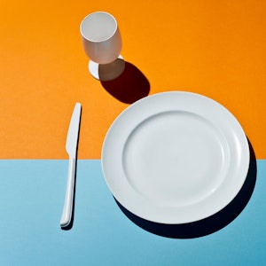 High Angle View Of white glass, fork, knife and plate on a colored table