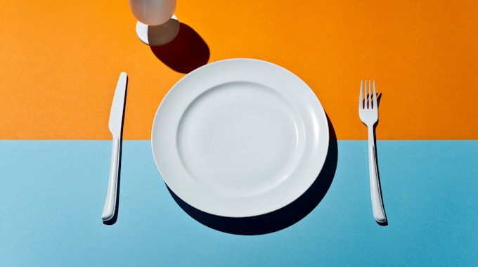 High Angle View Of white glass, fork, knife and plate on a colored table