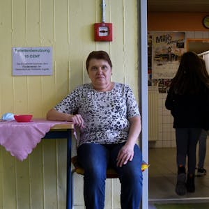 Eine Frau sitzt an einem Tischchen vor einer Toilettenanlage.
