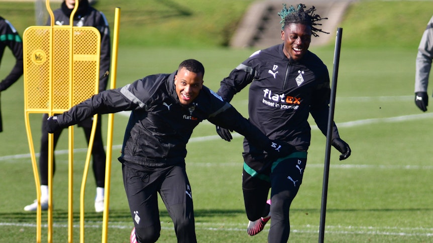 Gute Laune im Training von Borussia Mönchengladbach! Alassane Plea (l.) und Manu Koné liefern sich am 1. März 2023 ein Laufduell auf dem Trainingsplatz im Borussia-Park. Beide Spieler tragen dunkle Gladbach-Trainingskleidung und lachen beim Laufen.