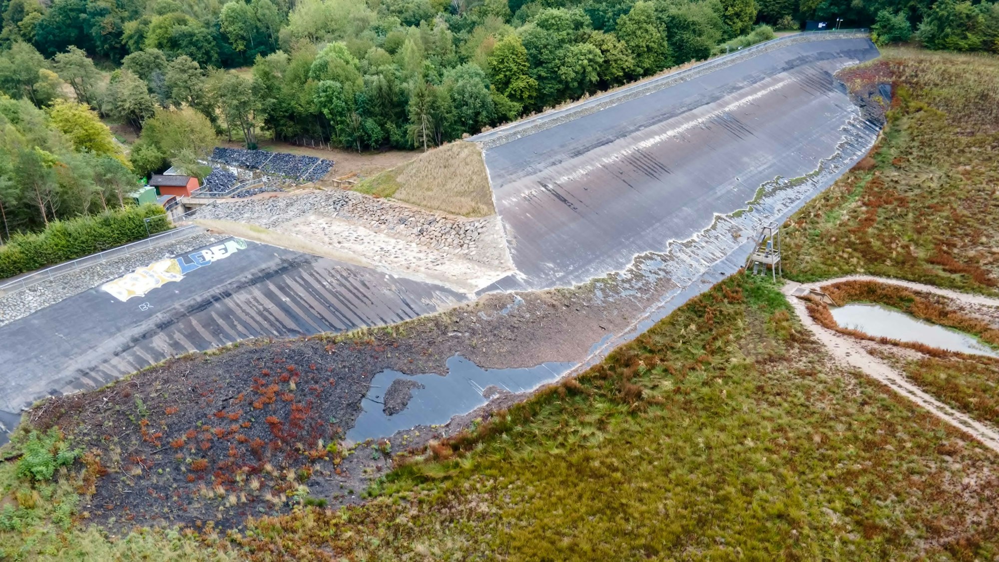 Das Bild zeigt den Damm der Steinbachtalsperre aus der Luft. Die Scharte in der Mitte ist deutlich zu erkennen.