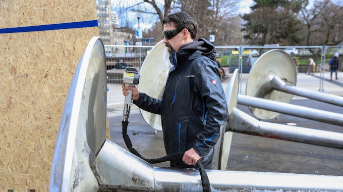 Ein Mann mit Schutzbrille reinigt das Kunstwerk „Wasserkinetische Plastik“ am Ebertplatz mit einem Lasergerät.