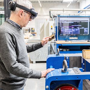 Ein Mann steht an einem Arbeitsplatz in einer Fabrikhalle. Er trägt eine Datenbrille.